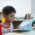 Braincore A young boy engrossed in reading a book in a classroom environment, promoting child literacy.
